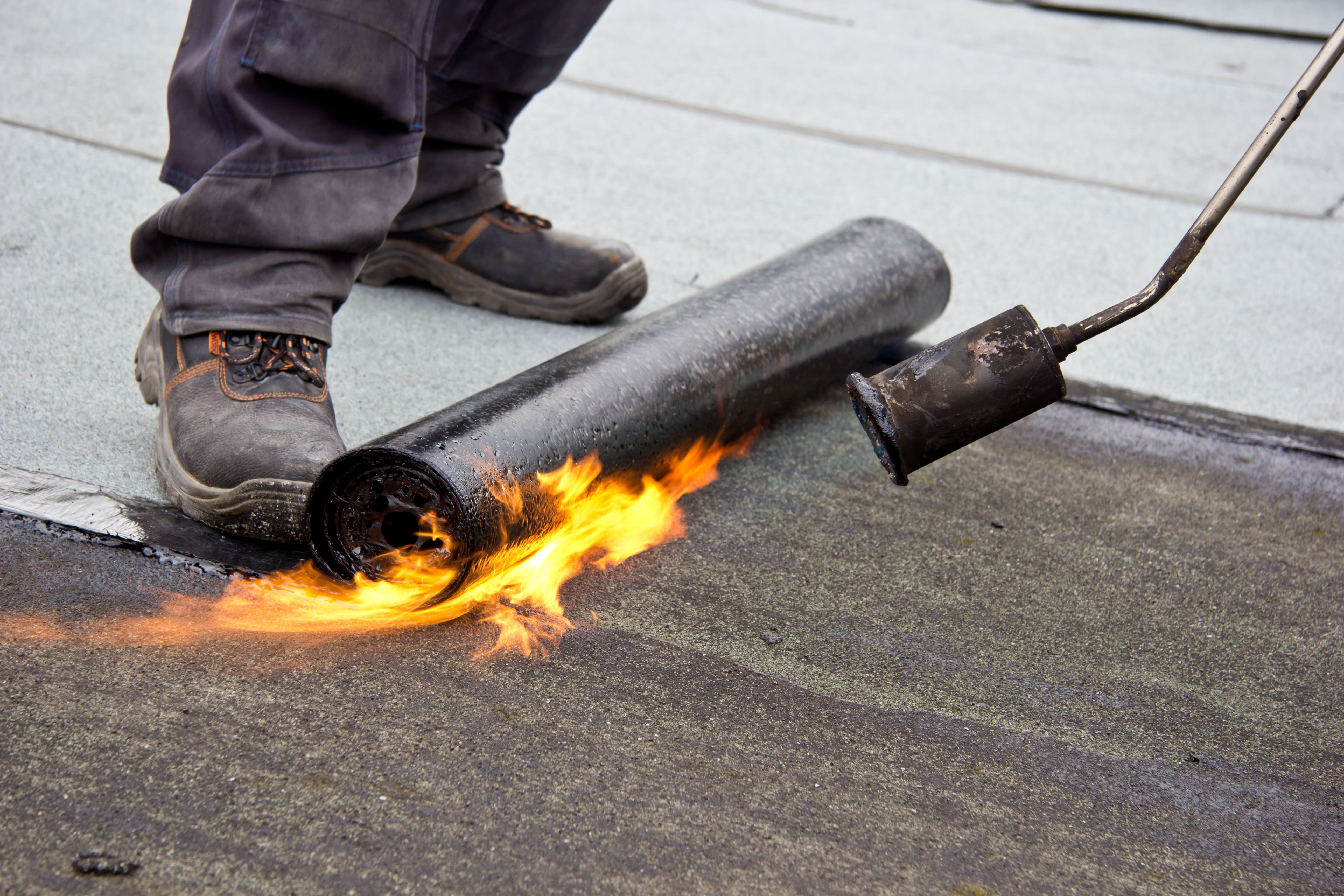 Flachdach wird mit Bunzenbrenner abgedichtet - man sich einen Flamme und die beine eines Dachdeckers